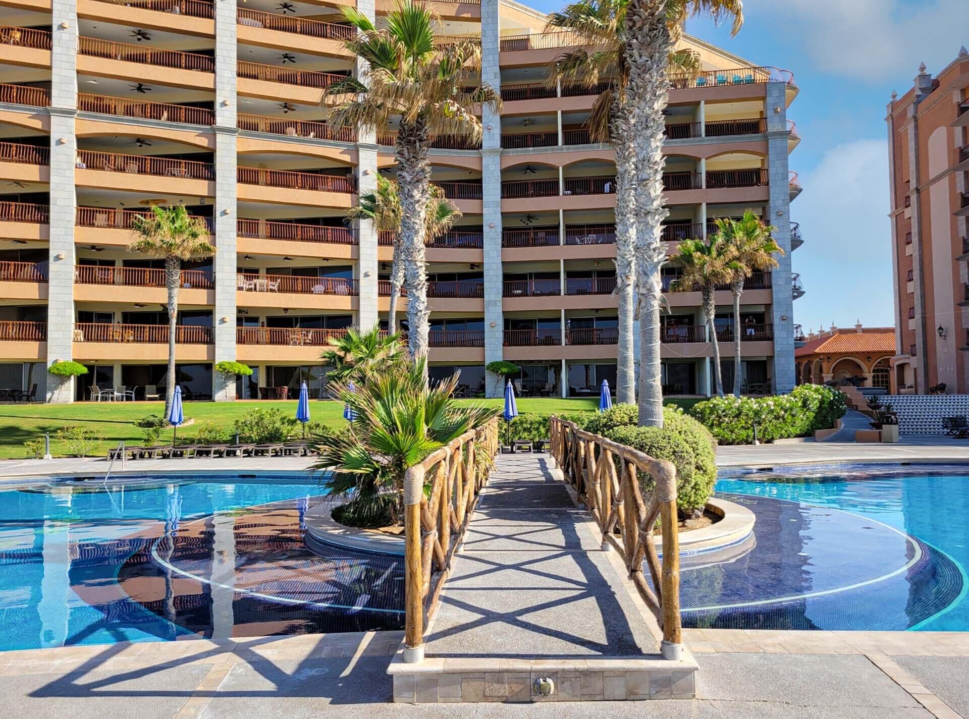 A hotel with multiple balconies, a swimming pool, and palm trees.