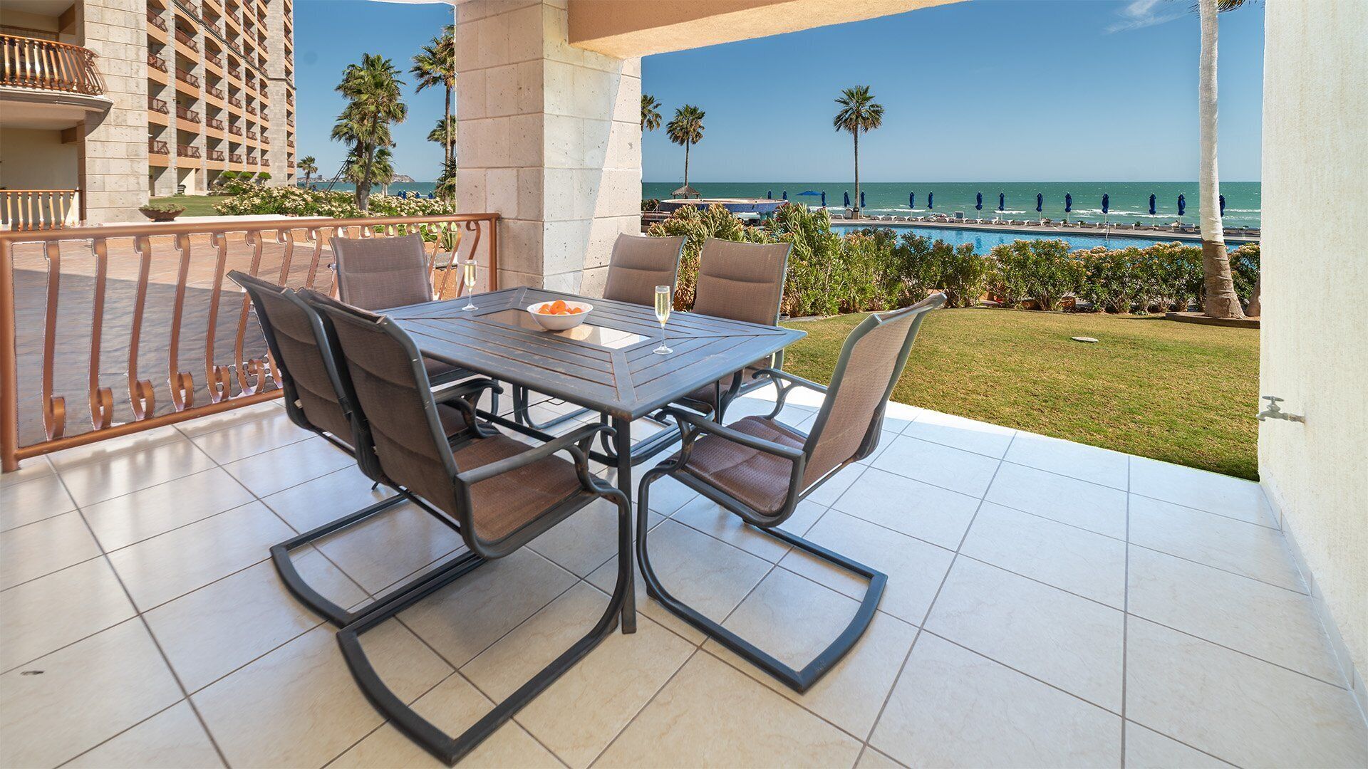 Une terrasse extérieure avec une table et des chaises, une vue sur l’océan et un bâtiment en arrière-plan.