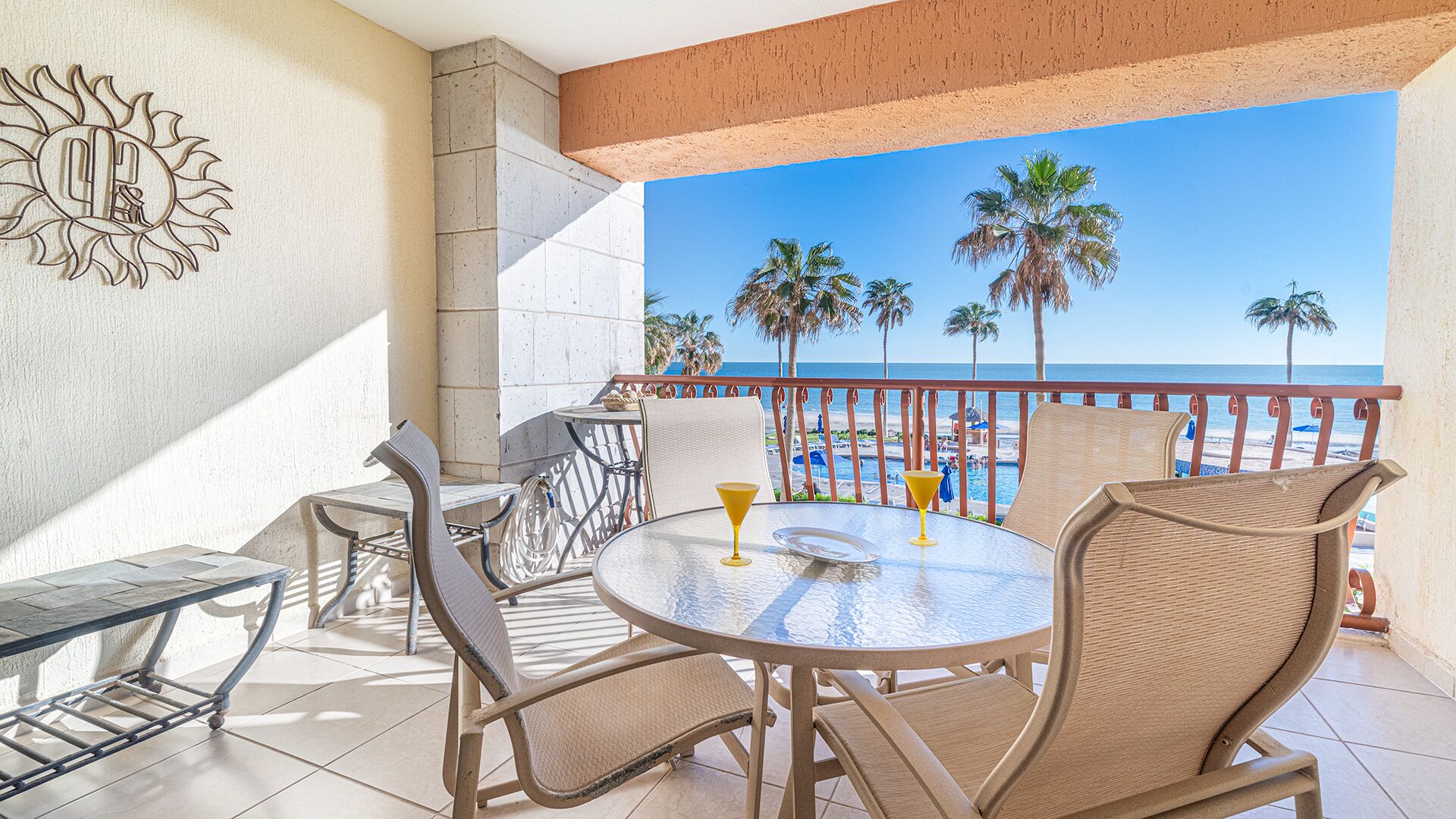 A balcony with a glass table, wicker chairs, and a view of the beach and ocean.