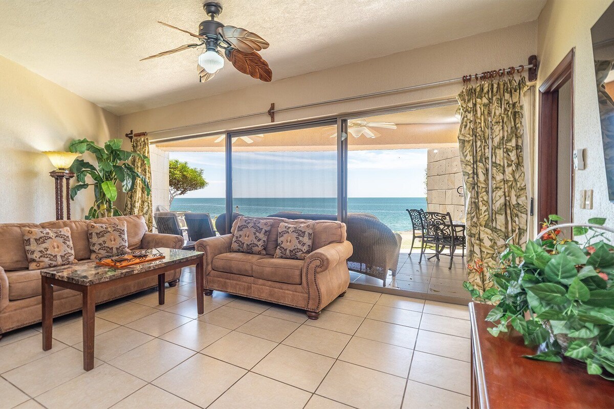A living room with a sofa set, a coffee table, and a view of the ocean through large glass doors.