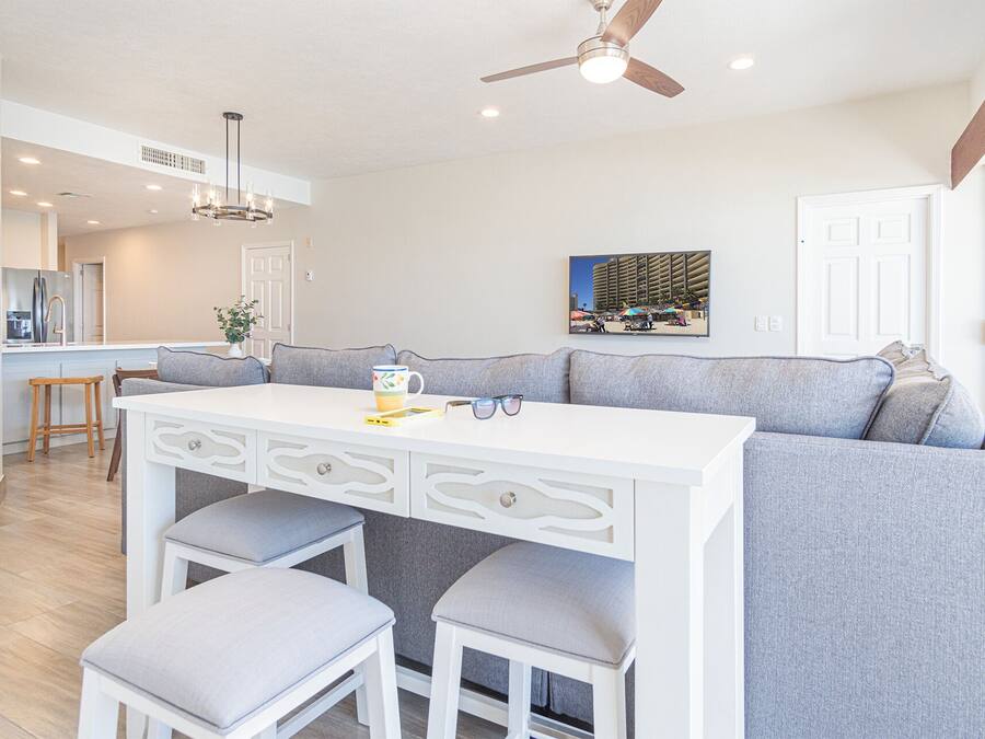A modern kitchen with a white island, grey seating, and a ceiling fan.