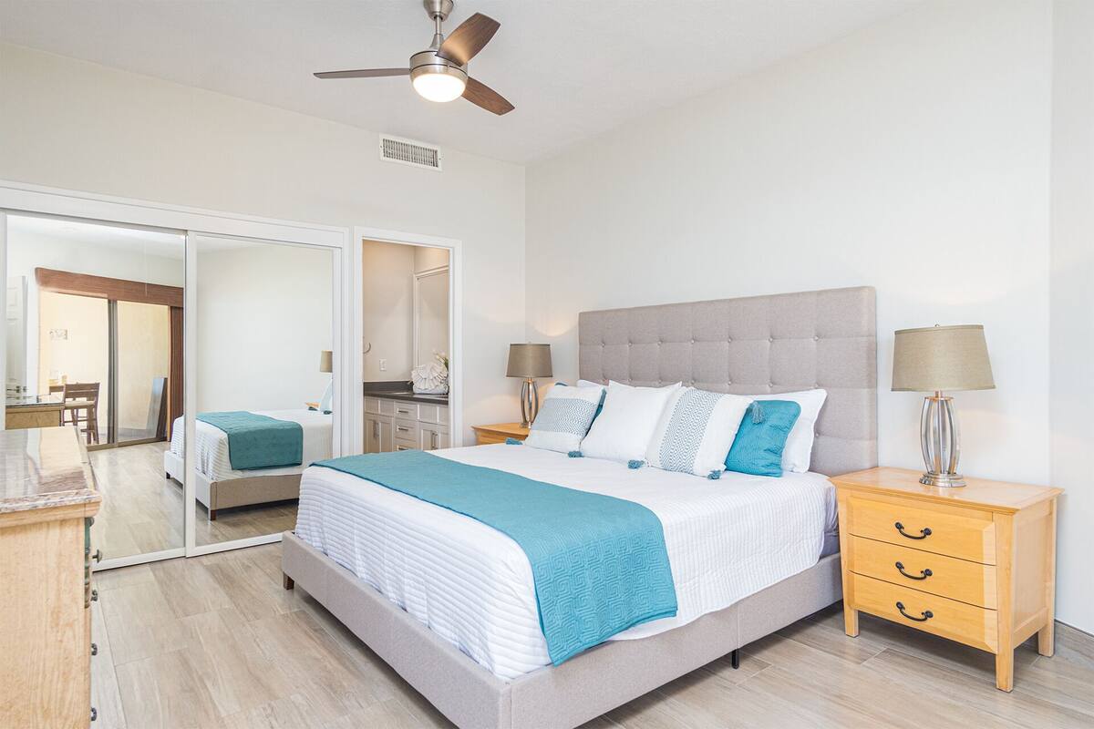Une chambre moderne avec un grand lit, des tables de chevet, un ventilateur de plafond et une porte coulissante donnant sur un balcon.