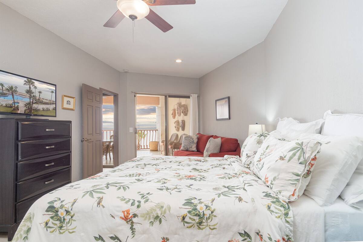 Une chambre à coucher comprenant un lit, une commode, un ventilateur de plafond et un balcon avec des chaises et une table.
