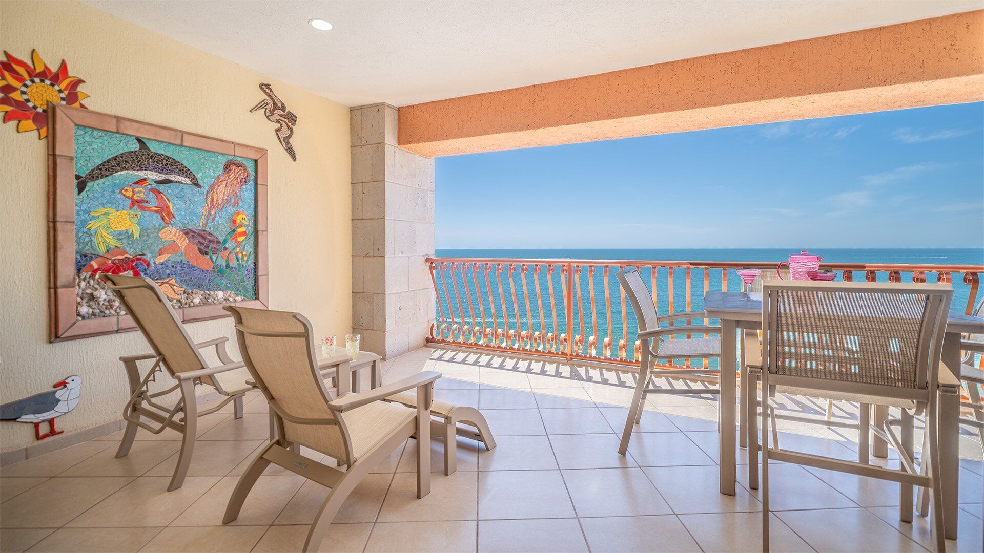 Ein Balkon mit Blick auf den Ozean, ausgestattet mit Stühlen und einem Tisch, verziert mit einem Mosaikkunstwerk.