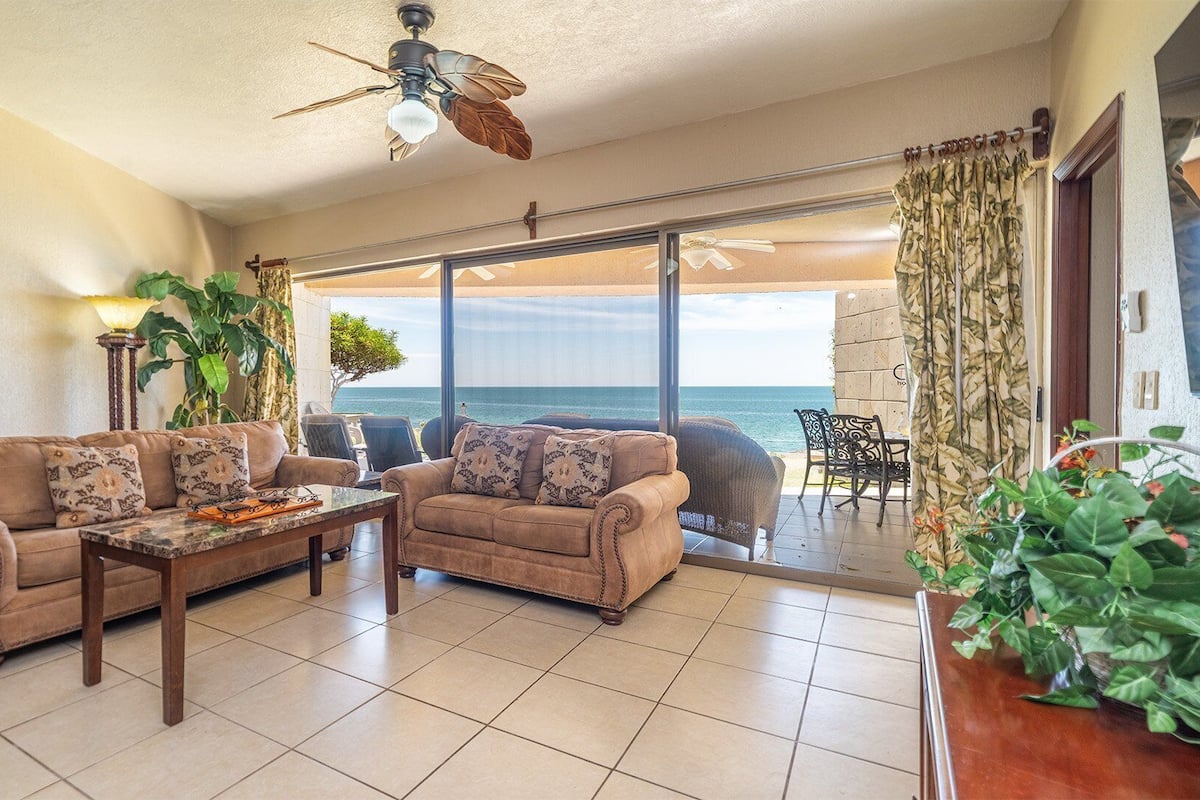 A living room with a sofa set, a coffee table, and a view of the ocean through large glass doors.