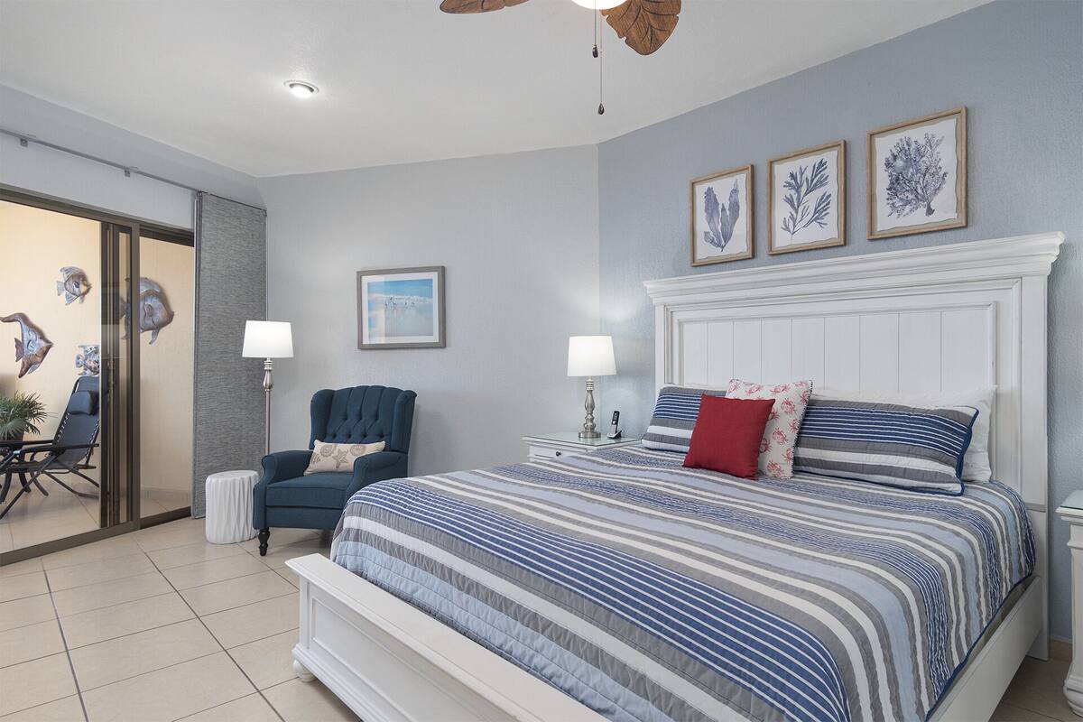 A bedroom with a large bed, two bedside tables, a chair, and a ceiling fan.