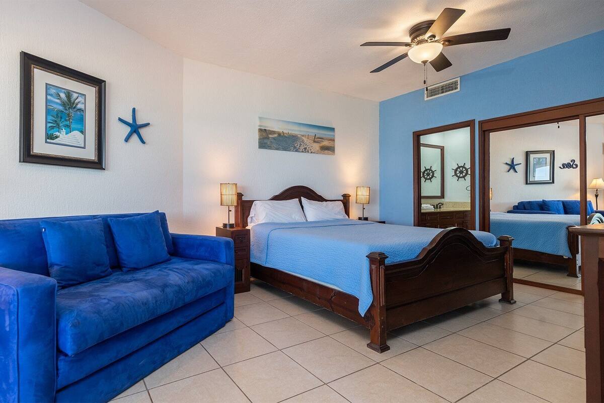A bedroom with a blue sofa, a wooden bed, and a ceiling fan.