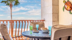 A balcony with a view of the sea, a table with a bowl of chips, a green glass, and a blue glass.