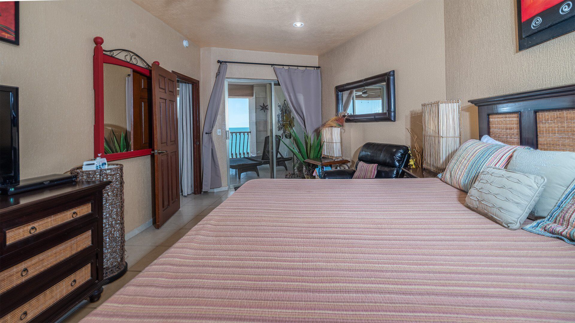 Un dormitorio con una cama grande, un aparador de madera, un televisor y un balcón con vistas.