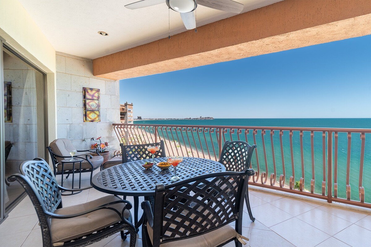 A balcony with a table and chairs, a view of the sea, and a railing.