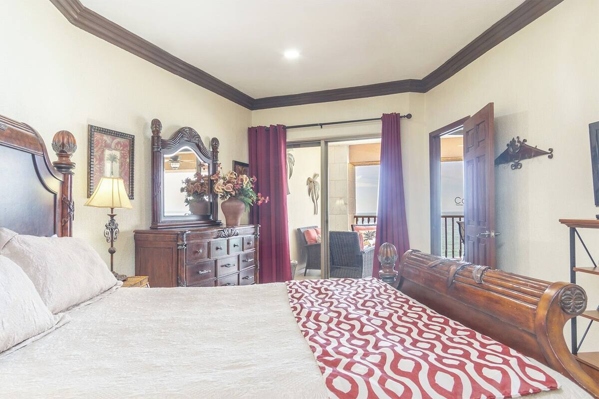 A bedroom with a large bed, a dresser, a mirror, and a window with curtains.