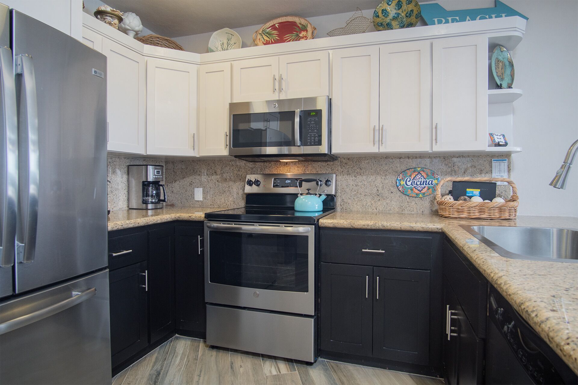 A kitchen with white cabinets, a stainless steel refrigerator, a microwave, a stove, and a sink.