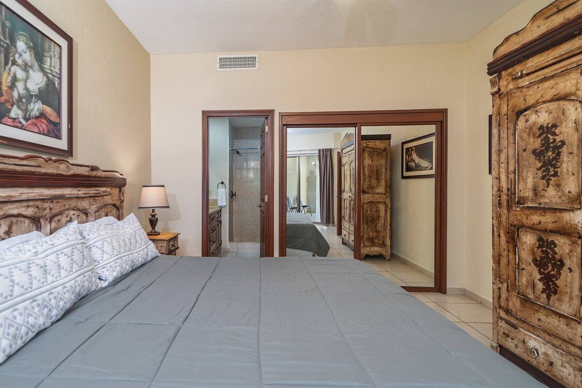 A hotel room with a large bed, a wooden headboard, a nightstand with a lamp, and a wardrobe.