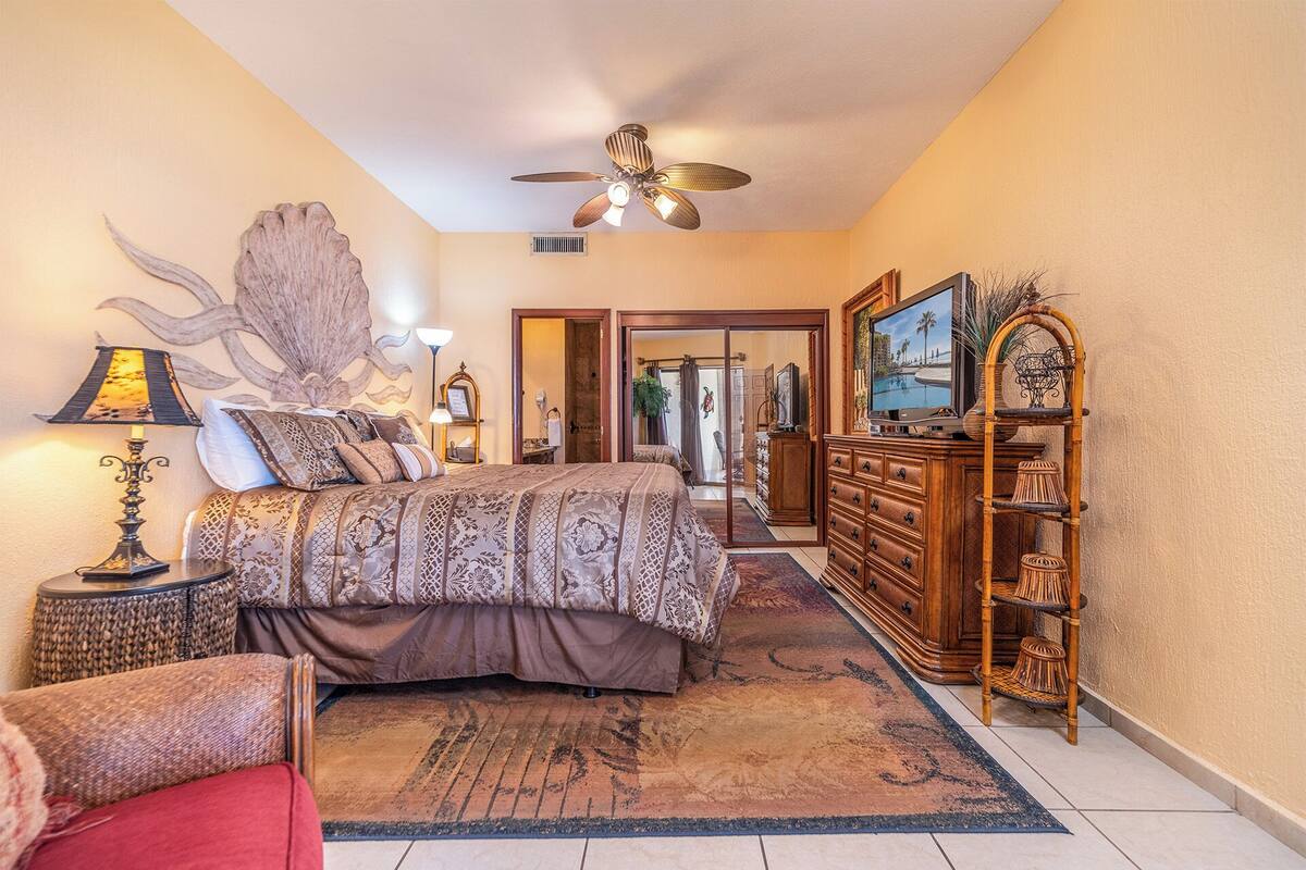A bedroom with a bed, a dresser, a television, and a ceiling fan.