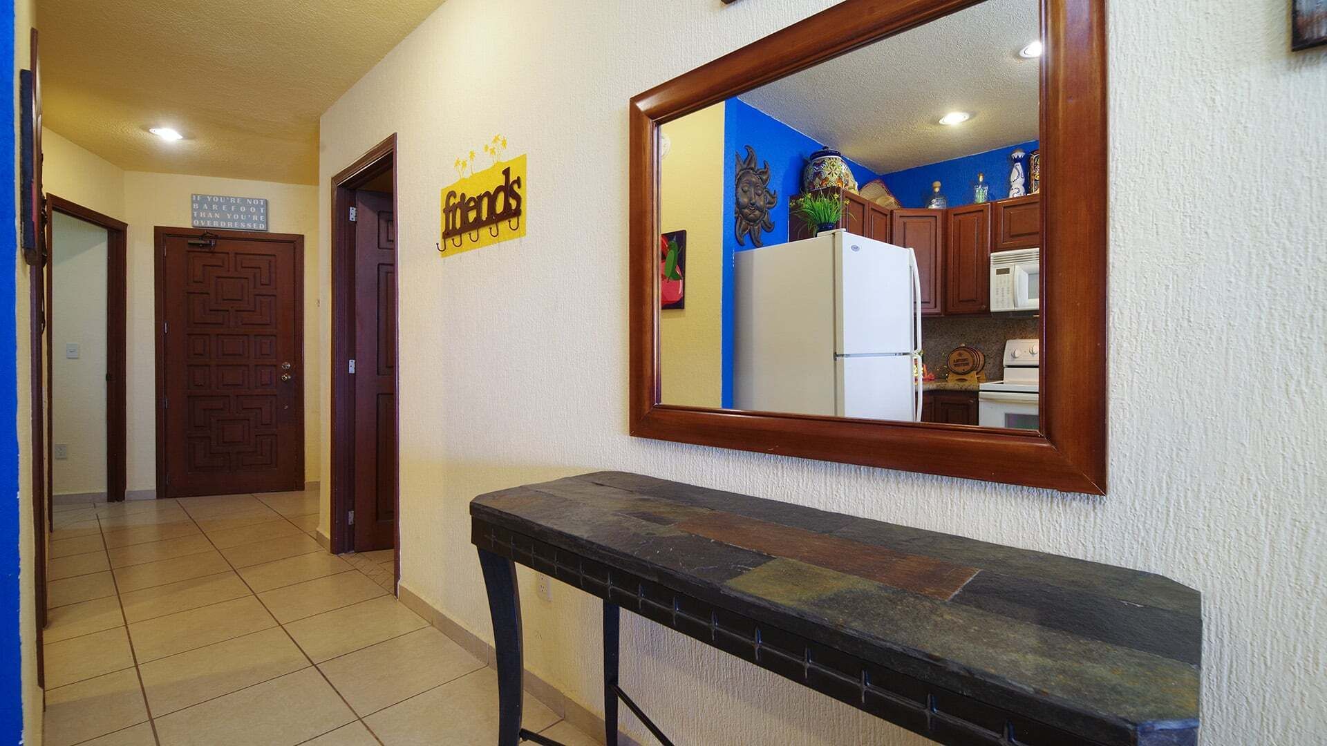 Een gang met een bank, een spiegel die een keuken reflecteert, en een bordje met de tekst 'vrienden' aan de muur.