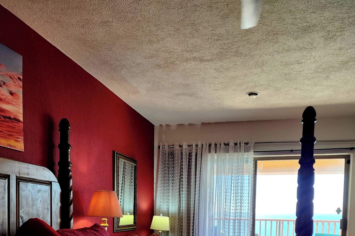 Une chambre d’hôtel avec un grand lit, une table de chevet, une lampe, un tableau au mur et une vue sur le balcon extérieur.