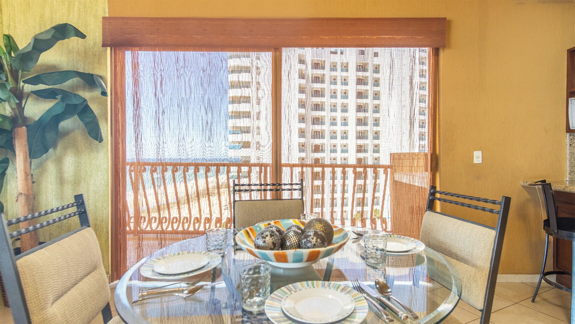 A dining area with a glass table, chairs, and a bowl of snacks.