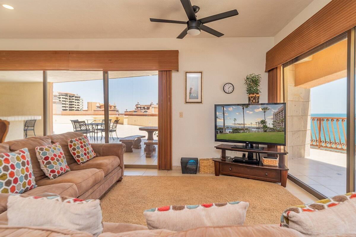 Un salon avec un canapé, une télévision et un balcon offrant une vue sur la mer.