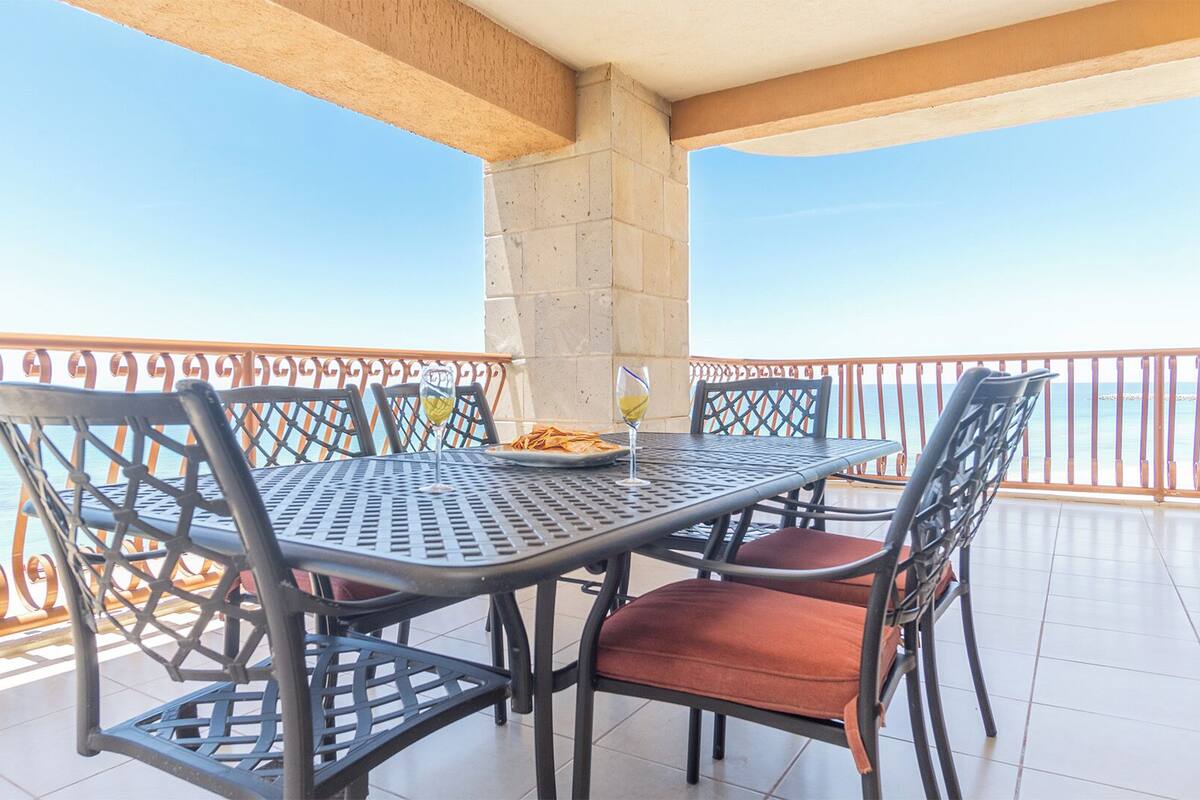A balcony with a table and chairs, a view of the sea, and a stone pillar.