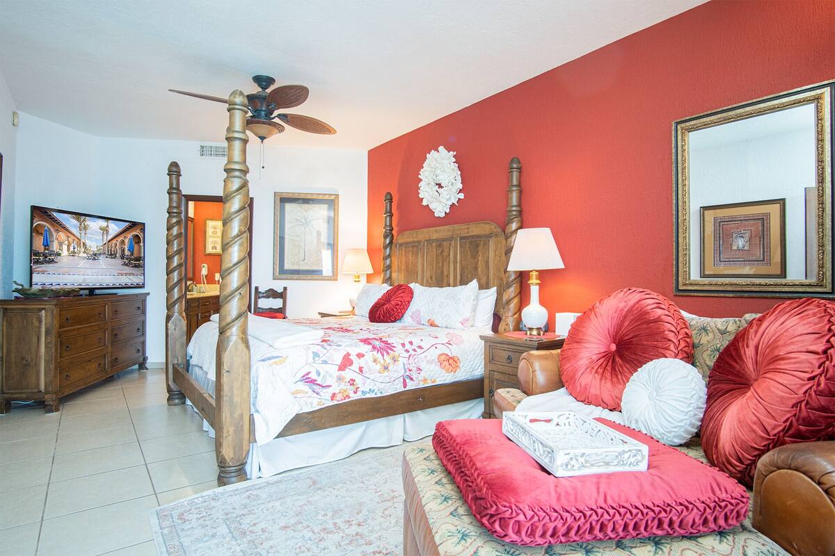 Une chambre à coucher avec un lit à baldaquin, une télévision, une table de chevet en bois, un mur rouge et un miroir.