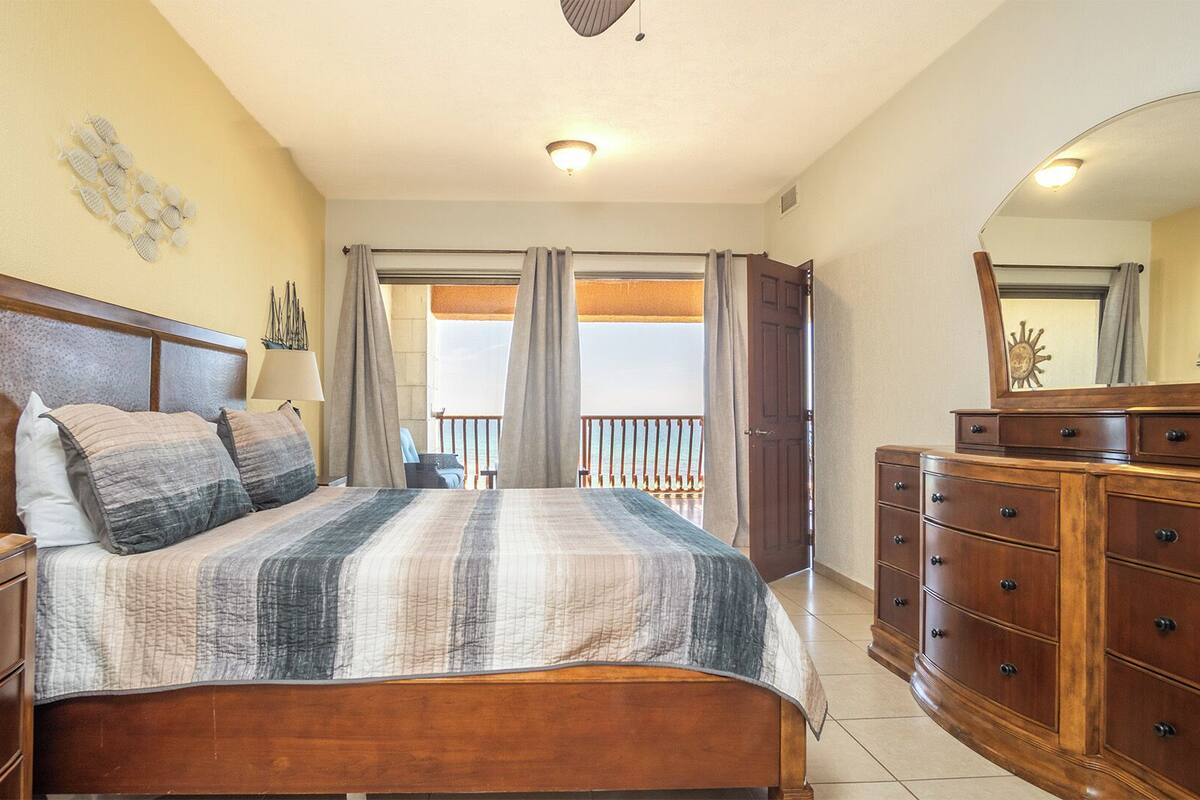 Une chambre avec un lit, une commode, un miroir et une vue sur le balcon.