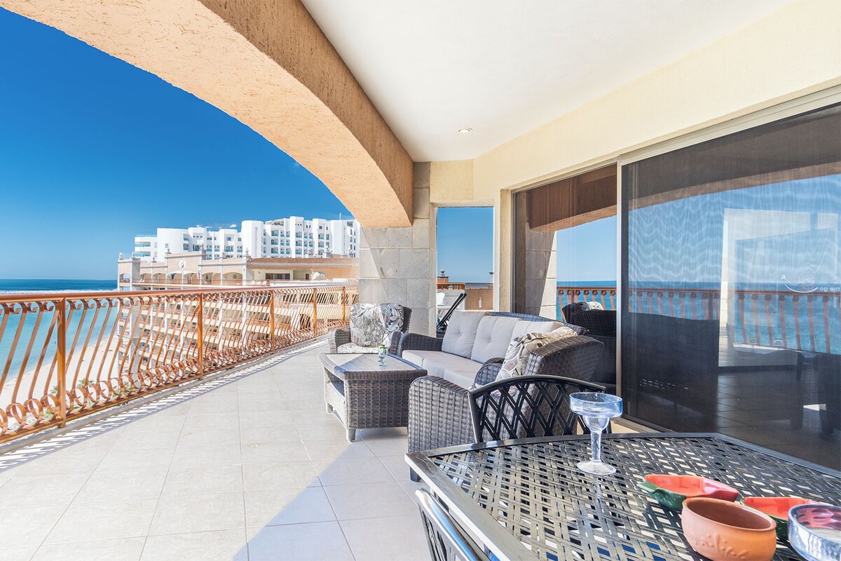 Un balcon avec vue sur la mer et les bâtiments, aménagé avec des fauteuils en osier et une table en verre.