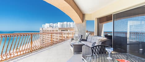 Ein Balkon mit Blick auf das Meer und Gebäude, ausgestattet mit Korbmöbeln und einem Tisch mit einem Glas.