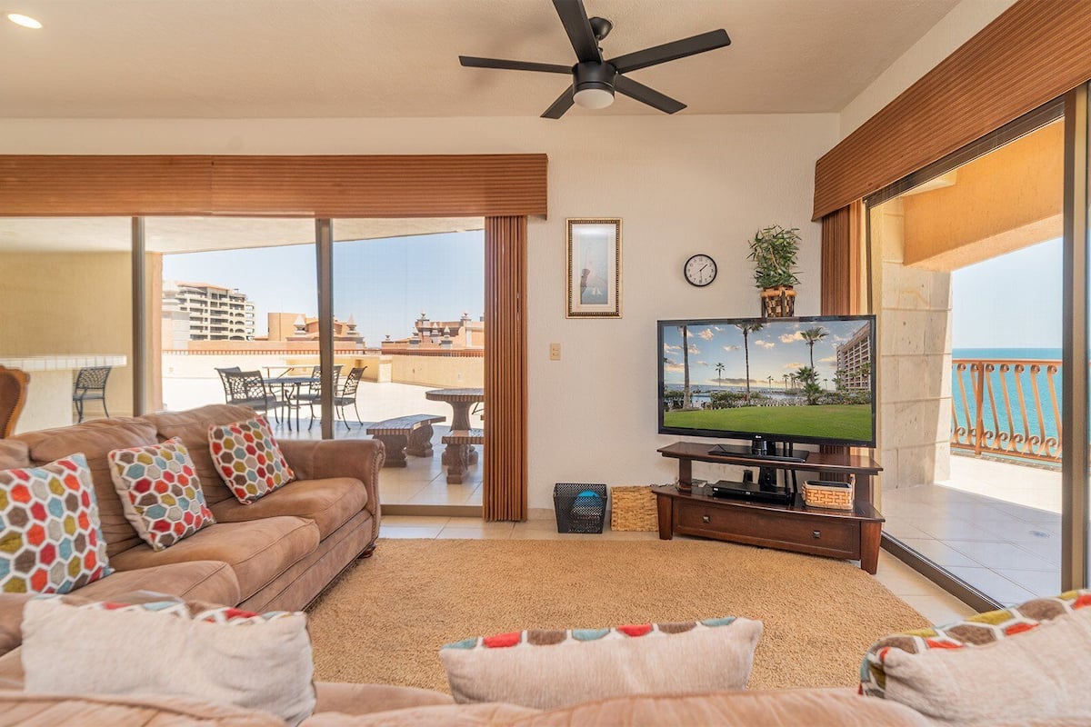 A living room with a sofa, TV, and a balcony with a view of the sea.