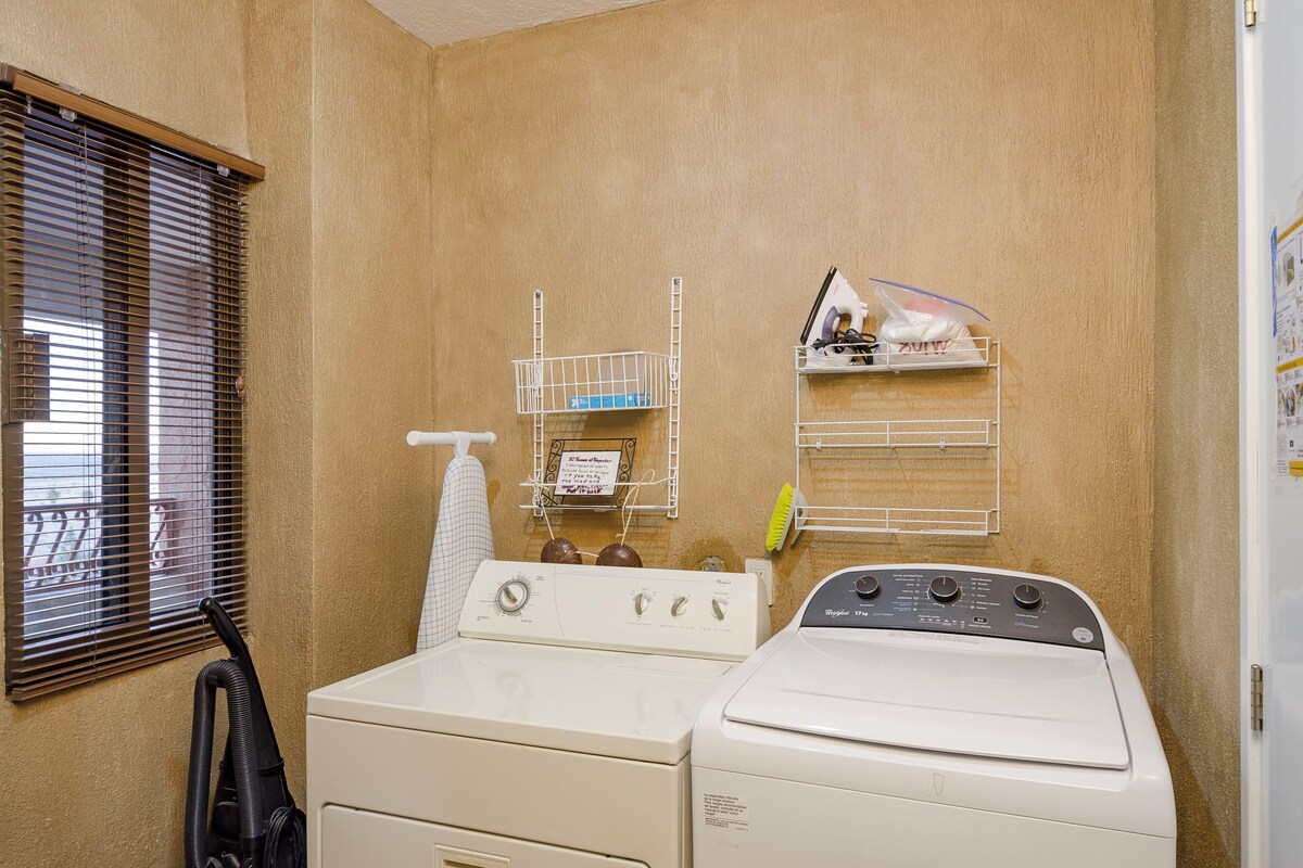 A laundry room with two washers and dryers, a drying rack, and a window with blinds.