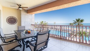 Ein Balkon mit Tisch, Stühlen, einer Wanddekoration in Sonnenform und Blick auf Pool und Strand.