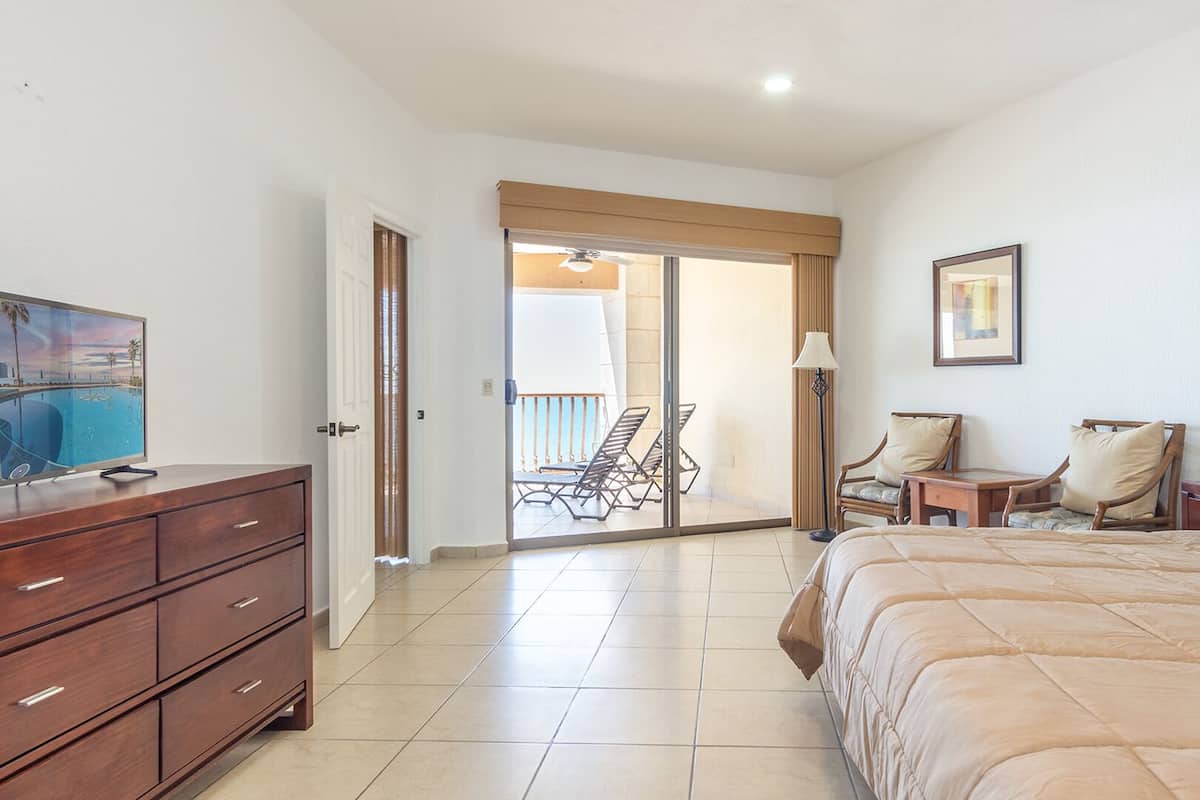 Une chambre d’hôtel équipée d’un lit, d’une télévision, d’un bureau et d’une chaise. Une porte coulissante donne accès à un balcon avec vue sur la piscine.