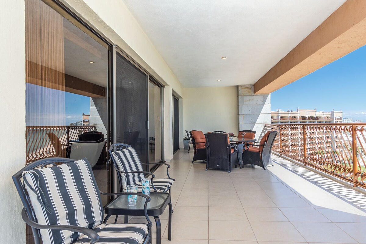 A balcony with chairs and a table, a sliding glass door, and a view of the beach.