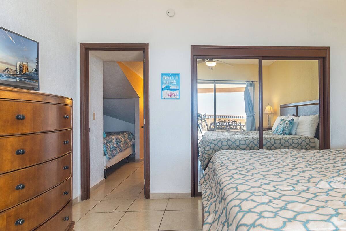 A hotel room with a bed, a dresser, and a view of the beach through a sliding door.