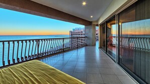 A balcony with a view of the sea, a tiled floor, and a bed with a yellow cover.