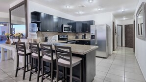 A modern kitchen with dark cabinets, a central island with bar stools, a microwave, a refrigerator, and a water dispenser.