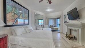 A spacious bedroom with a large bed, a ceiling fan, a flat-screen TV, and a fireplace.