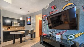 A modern kitchen with a microwave, a dining table, and a TV wall-mounted above a black entertainment unit.