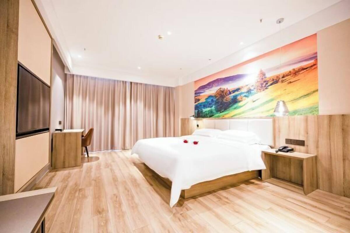 Une chambre d’hôtel moderne avec un grand lit, un bureau, une chaise et un tableau au mur.