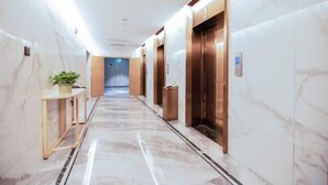 A hallway with marble flooring, wooden paneling, and two elevators. - Qingdao Likelai Garden Hotel (Chengyang Zhengyang Middle Road Metro Station) (Qingdao)