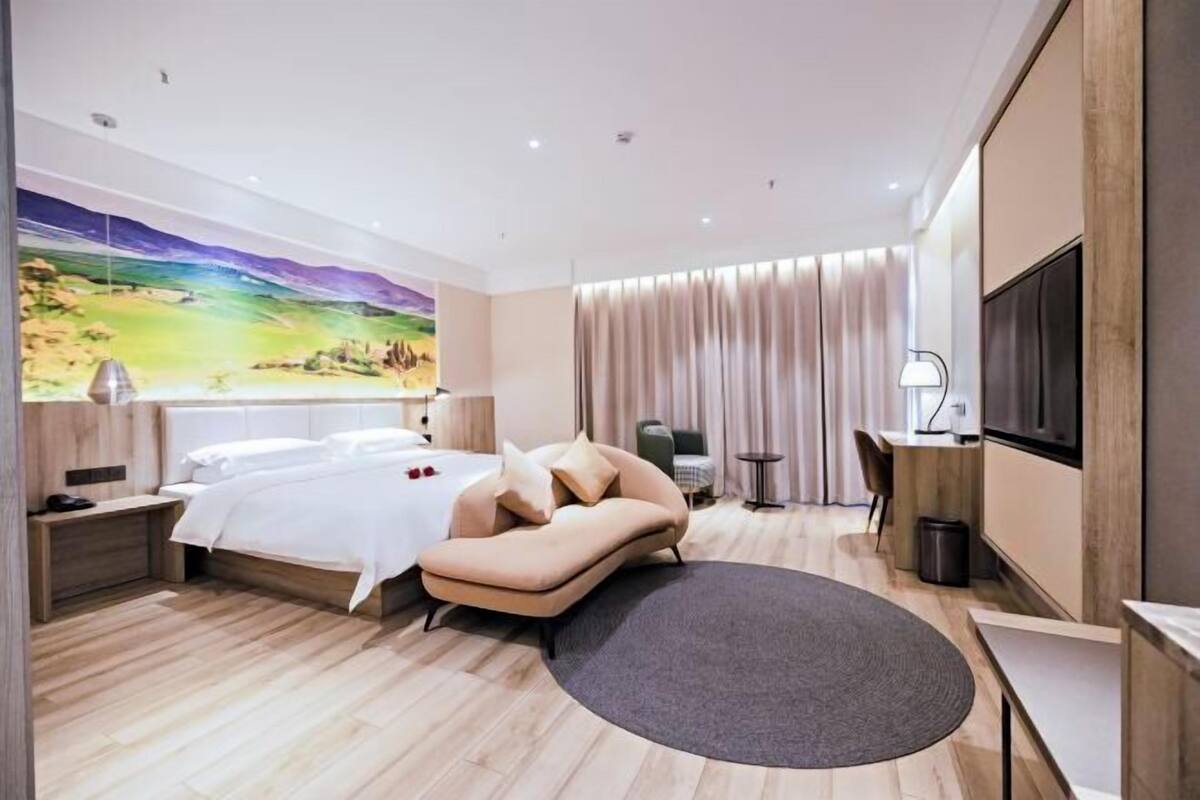 Une chambre d’hôtel moderne, équipée d’un lit, d’un canapé, d’un bureau, d’une télévision et ornée d’un tableau au mur.