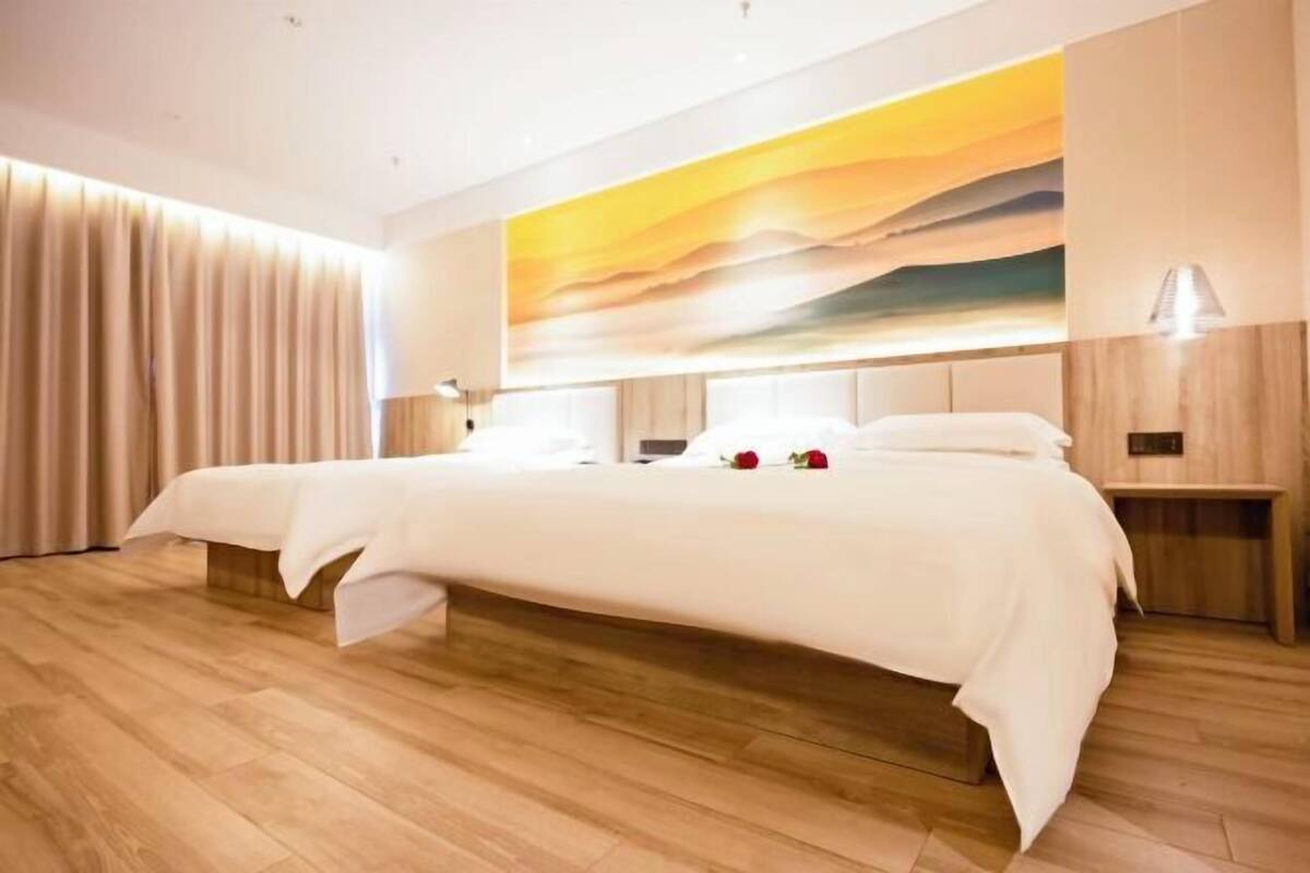 Une chambre d’hôtel moderne avec un grand lit, un parquet en bois, une grande peinture abstraite au mur et une table de chevet avec une lampe.