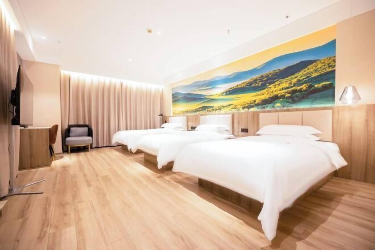 Une chambre d’hôtel avec trois lits, un grand tableau représentant un paysage, un bureau et une chaise.