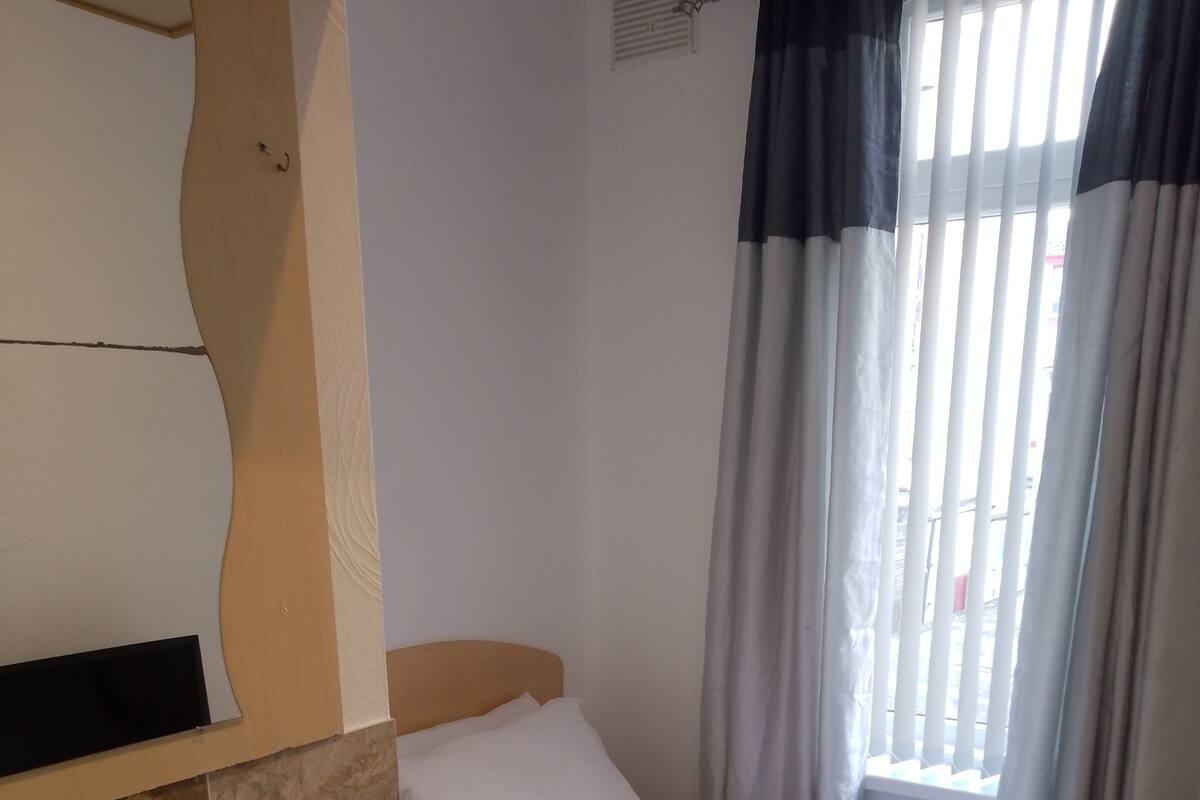 A small, neatly arranged bedroom with a single bed, a bedside table, and a window with curtains.
