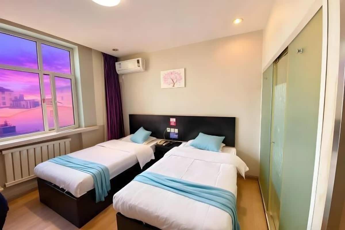 Une chambre d’hôtel avec deux lits, une fenêtre donnant sur un beau paysage, un appareil de climatisation, une table de chevet et une œuvre d’art accrochée au mur.
