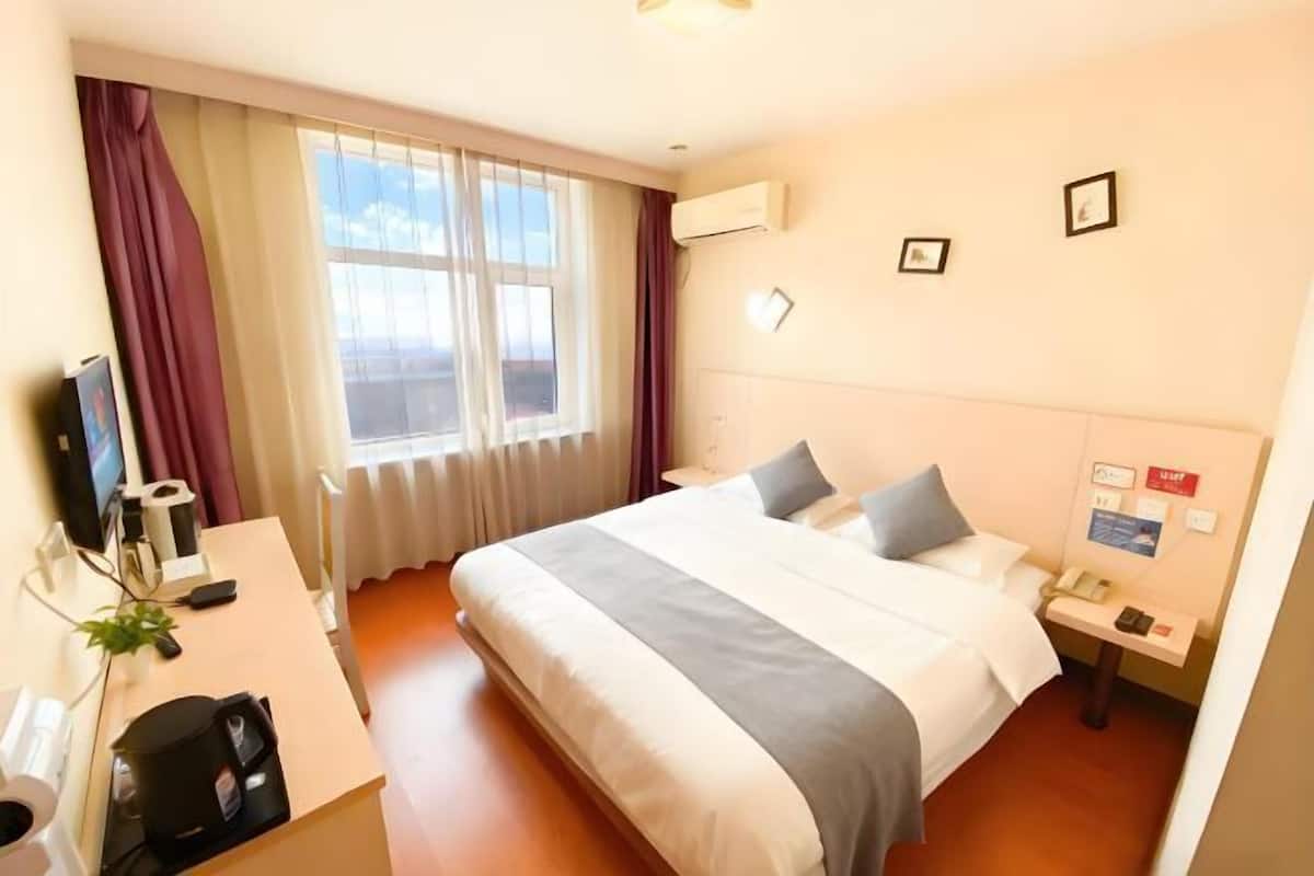 Une chambre d’hôtel avec un lit, un bureau, une chaise, une télévision et une fenêtre avec des rideaux.