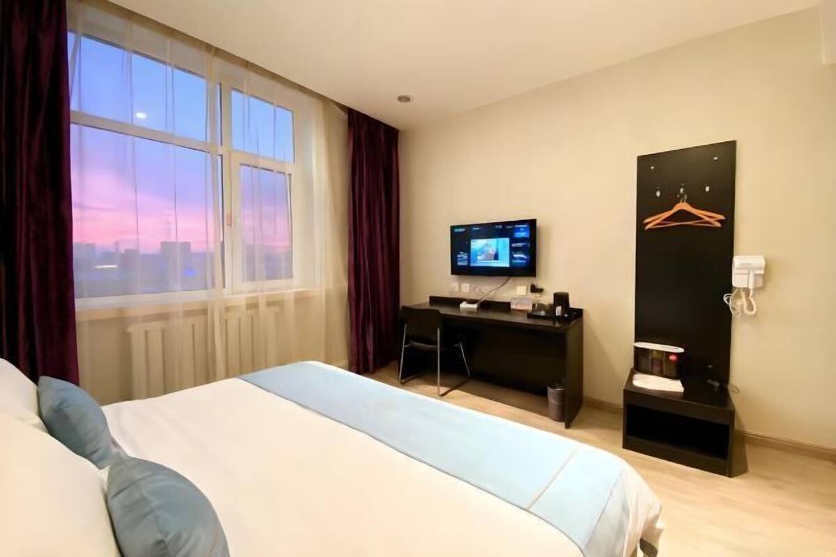 Une chambre d’hôtel équipée d’un lit, d’un bureau, d’une télévision et offrant une vue sur le paysage urbain.