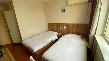 Et hotelværelse med to senge, en træsenggavl, en radiator og en dør til venstre.