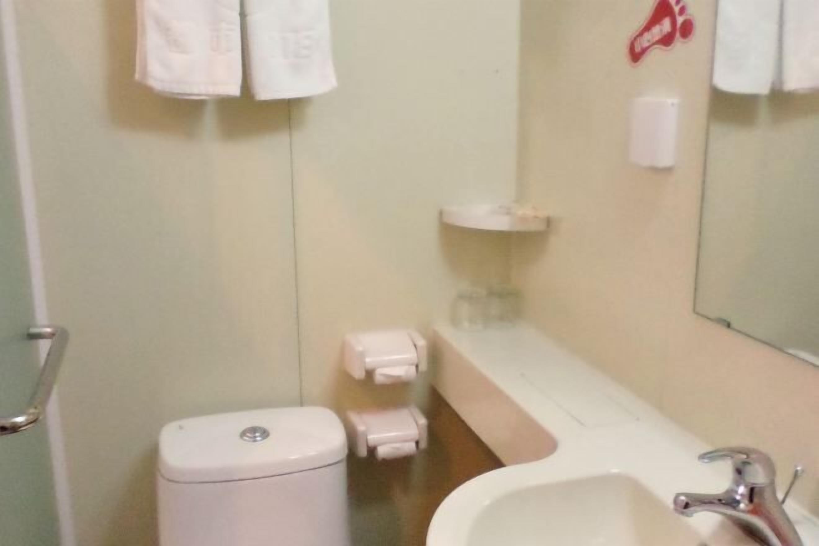 Ein Badezimmer mit Toilette, Waschbecken und Spiegel. Handtücher hängen an der Wand und eine Seifenspender ist vorhanden.