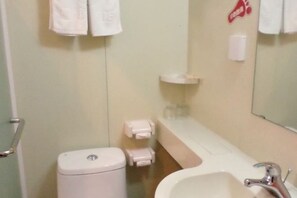 Un baño con inodoro, lavamanos y espejo. Hay toallas colgadas en la pared y un dispensador de jabón.