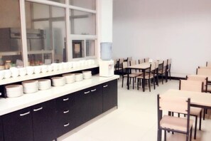 A dining area with tables and chairs, a counter with plates, and a window. - Gaocheng Dushi 118 Chain Hotel (Shijiazhuang)